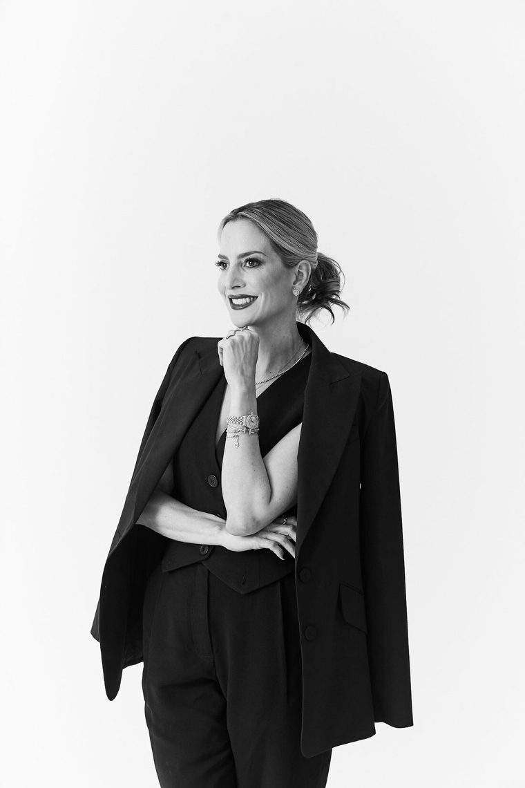 Karina Al Assal em retrato editorial, terno preto, fundo creme
