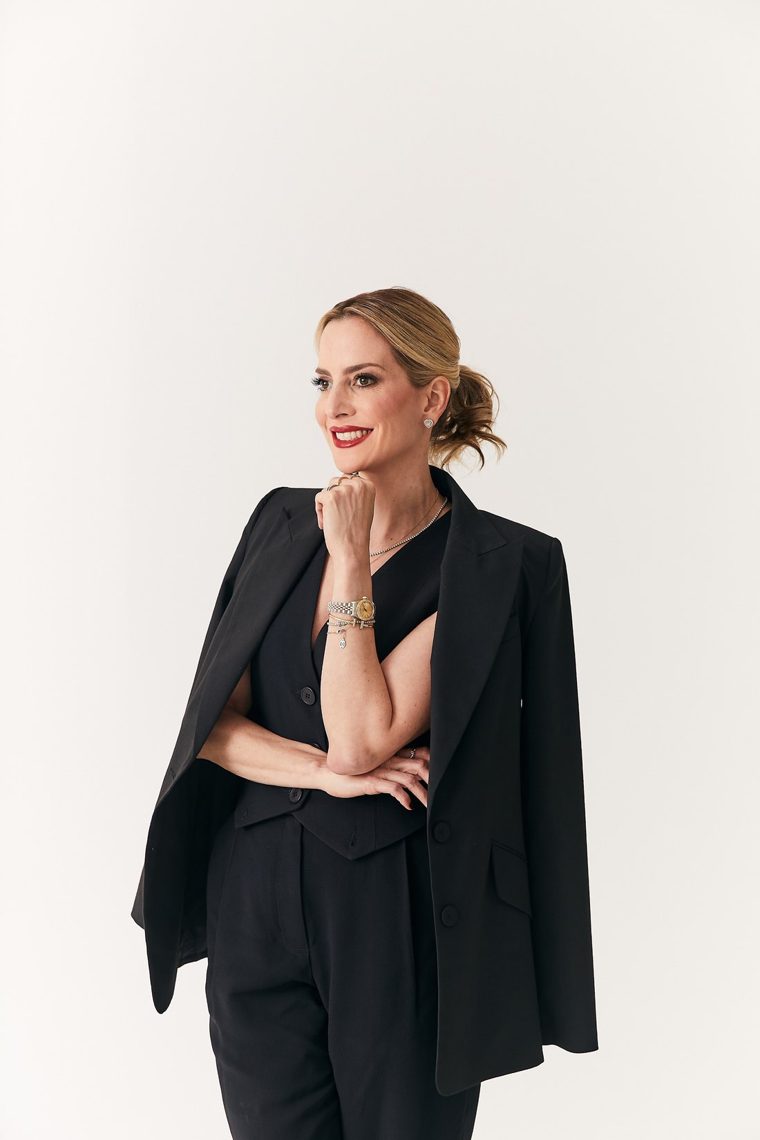 Karina Al Assal em retrato editorial, terno preto, fundo creme